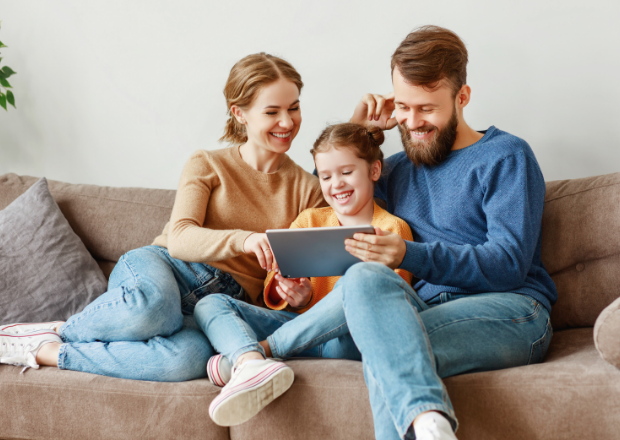 Mother and father sitting on the couch with daughter between them looking at a tablet